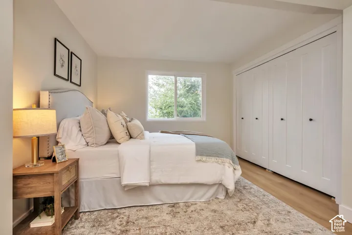 Serene primary bedroom featuring hardwood flooring, abundant natural light from large picture windows, built-in closet storage with multiple panels, warm ambient lighting from bedside fixtures, and a neutral color palette with layered bedding and coordina