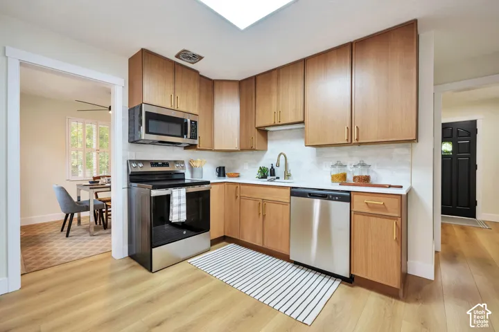 Modern kitchen featuring warm wood-finish cabinetry, stainless steel appliances including a built-in microwave and electric range, white subway tile backsplash, and wood-finish flooring throughout