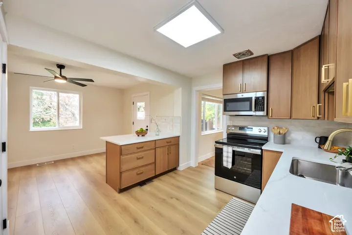 Modern kitchen featuring warm wood-finish cabinetry, stainless steel built-in appliances including double wall ovens, white quartz countertops, and a large center island with additional storage