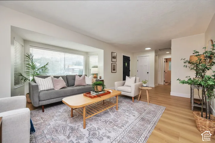 Bright living room featuring hardwood flooring, large bay window with plantation shutters, and neutral wall finishes