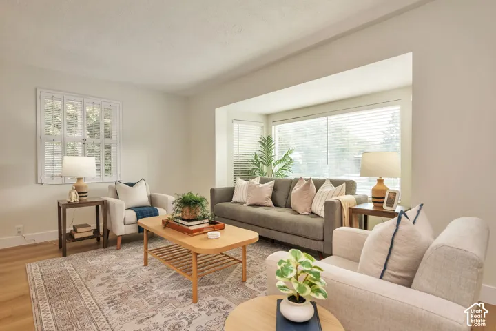 Bright, light-filled living room featuring expansive windows with plantation shutters, warm wood-finish flooring, and neutral wall tones