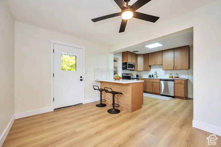 Open-concept kitchen and dining area featuring warm wood-finish cabinetry, stainless steel appliances, a central island with seating, and engineered wood flooring throughout