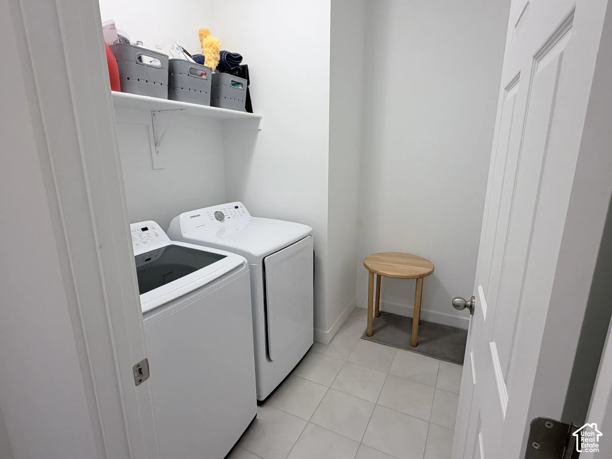 Laundry area with light-colored floor tile, a white wall-mounted shelf, and a white paneled door