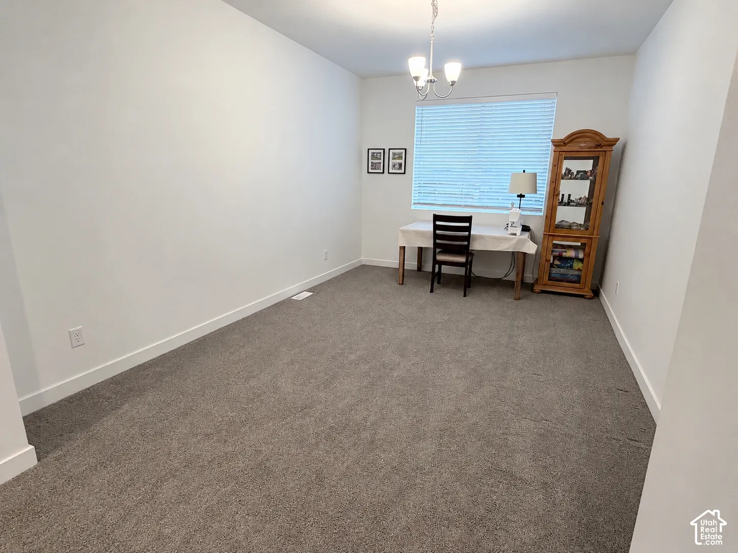 Recessed window with horizontal blinds, overhead chandelier, and neutral wall paint