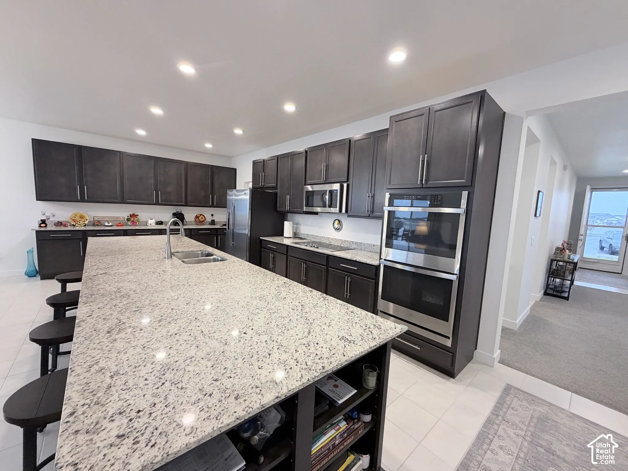 Spacious kitchen featuring an extended island with integrated sink, dark wood-finish cabinetry, stainless steel appliances, and recessed lighting