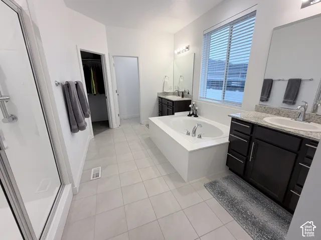 Spacious bathroom featuring a built-in soaking tub, dual dark wood-finish vanities with light stone countertops, a glass-enclosed shower, and tiled flooring