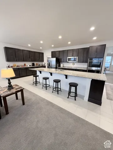 Spacious kitchen featuring dark flat-panel cabinetry, light granite-style countertops, stainless steel appliances, and an expansive breakfast bar with seating