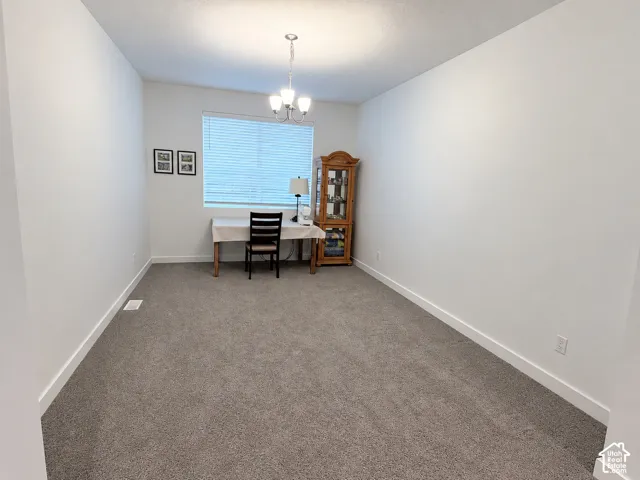 Carpeted room with a ceiling-mounted chandelier and a window featuring horizontal blinds