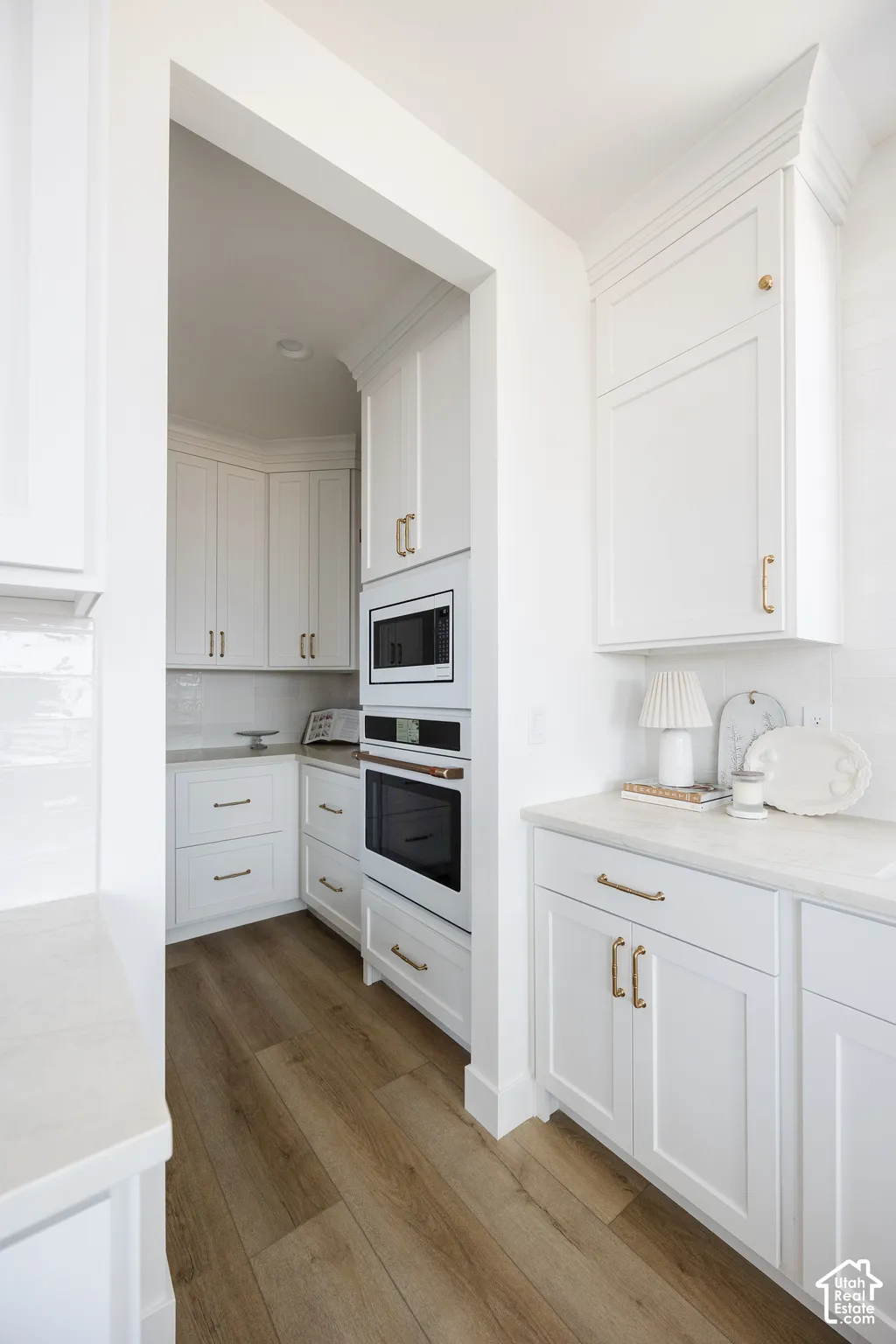 White shaker cabinetry, wood-finish flooring, integrated wall oven, integrated microwave, and white subway tile backsplash