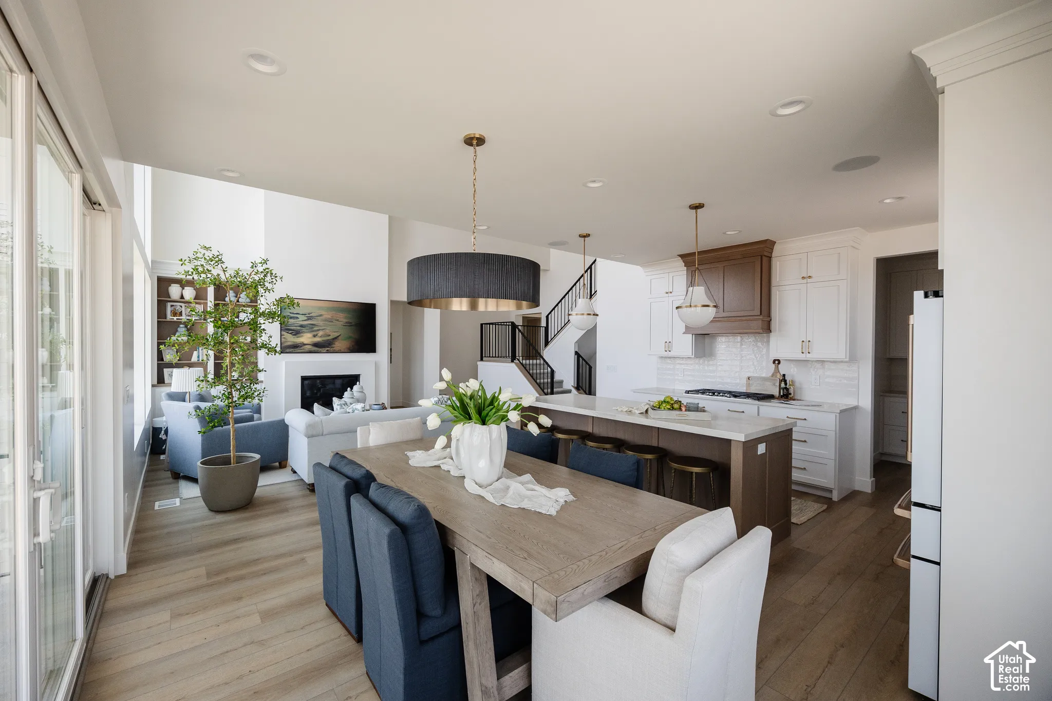 Open-concept living space featuring wood-finish flooring, a kitchen island with seating, white cabinetry, a white subway tile backsplash, and a fireplace with a mantel