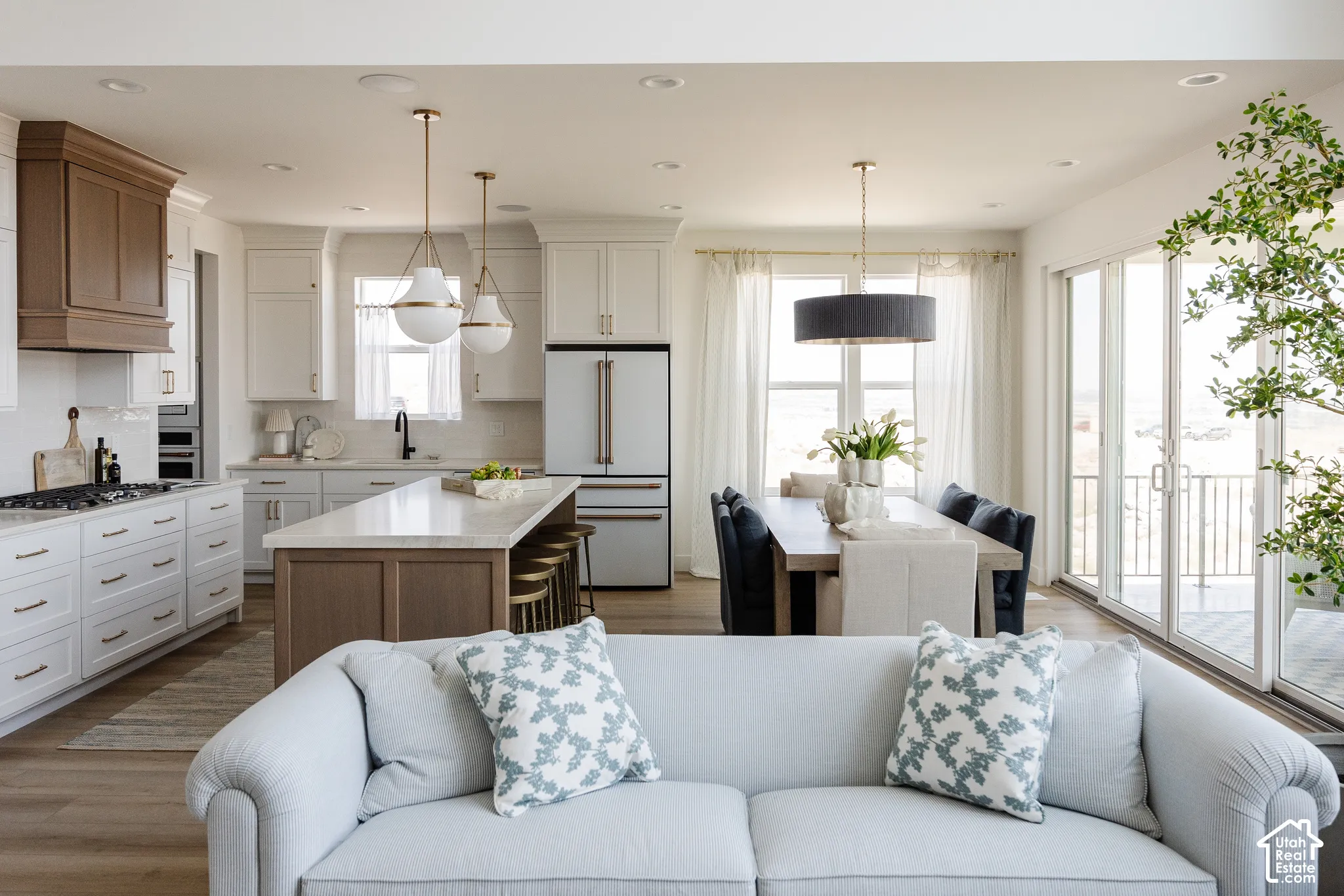 Open concept living area featuring wood-finish flooring, a kitchen island with seating, a dining area with expansive glass doors, and recessed lighting