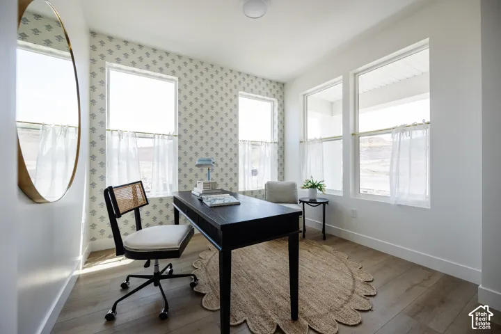 Wood-finish flooring, multiple windows, patterned accent wall, recessed ceiling lighting, and crisp white baseboards