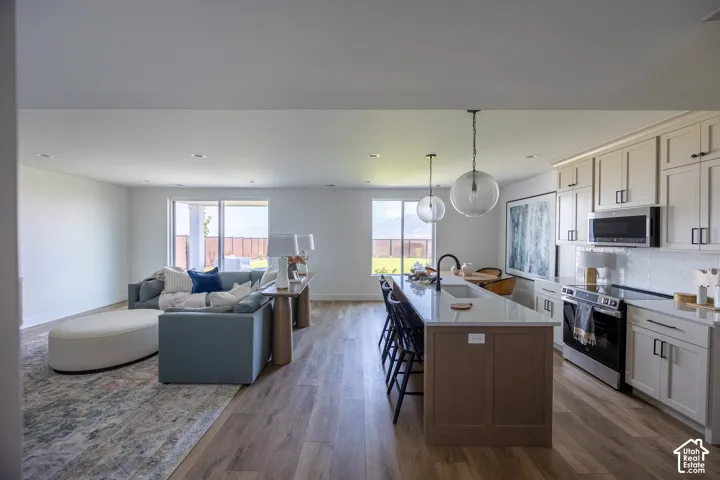 Open-concept living space featuring wood-finish flooring, a kitchen island with seating, pendant lighting, built-in cabinetry, and sliding glass doors
