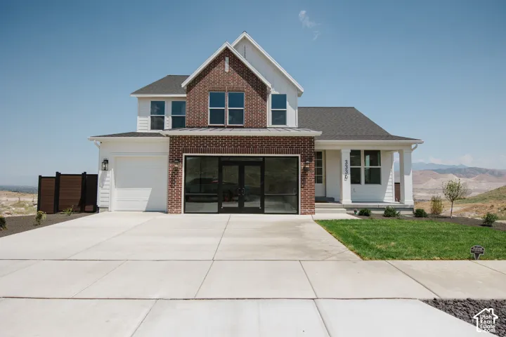 Contemporary two-story residence featuring brick and siding facade, an integrated garage with a modern glass door, a secondary garage with a white door, a covered entry porch with columns, and a concrete driveway