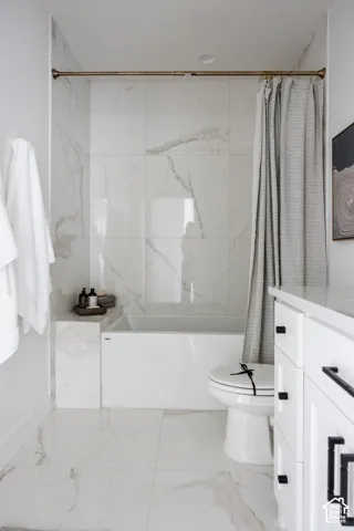White tiled flooring, a built-in bathtub, and a toilet with a white seat