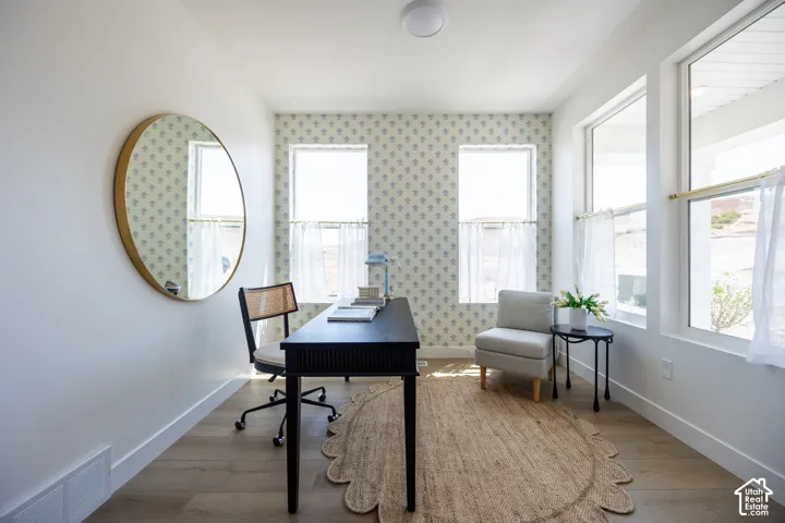 Wood-finish flooring, accent wall with patterned wallpaper, multiple windows with natural light, modern ceiling light fixture, and a large wall mirror