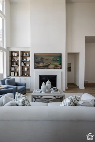 Two-story living area with high ceilings, large windows, built-in shelving, a fireplace, and wood-finish flooring