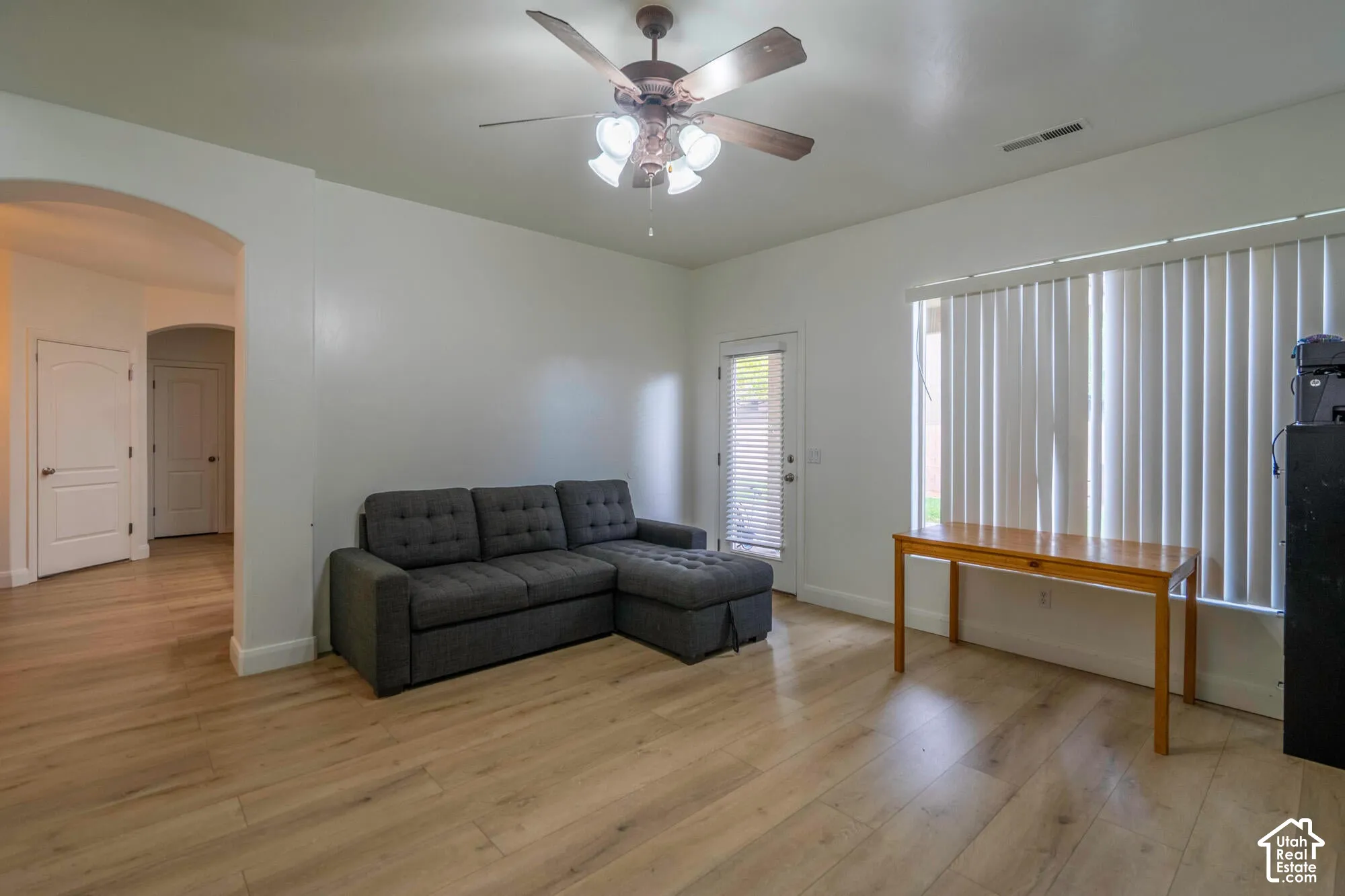 Spacious room featuring wood-finish flooring, an arched doorway, a ceiling fan with integrated lighting, and a glass-paneled exterior door