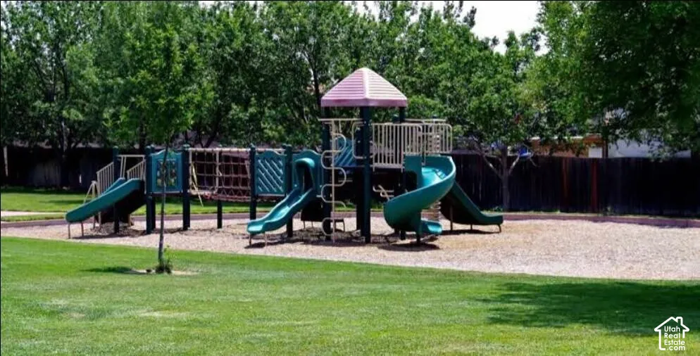 Recreational area featuring play structure with slides and climbing elements, surrounded by a wood chip surface and expansive green lawn