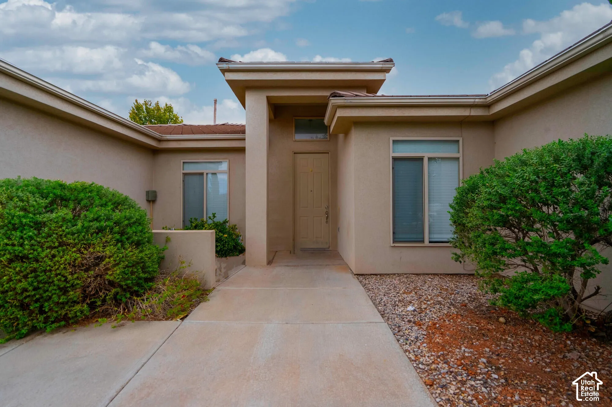 Stucco exterior with a covered entry, concrete walkway, and rock landscaping