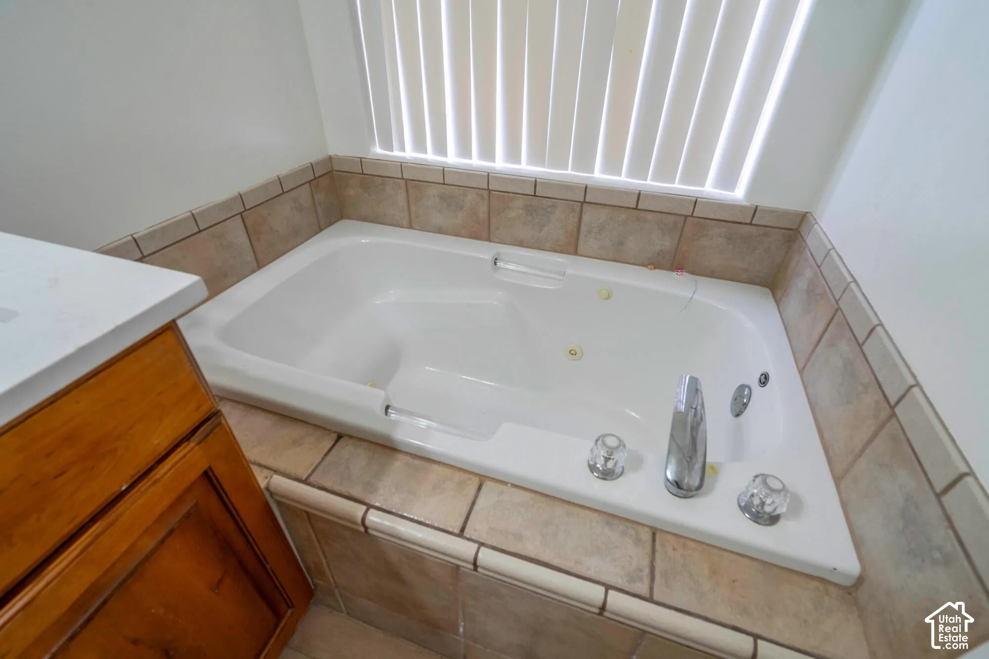White built-in soaking tub with chrome fixtures, surrounded by neutral-toned tiled decking and wall accents