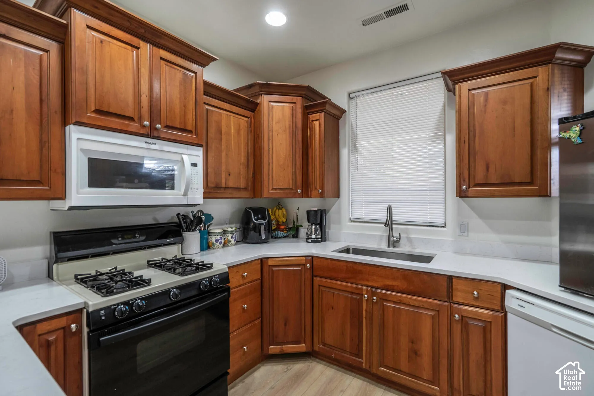 Wood-finish cabinetry, light-toned countertops, built-in microwave, gas range, and stainless steel sink with a high-arc faucet