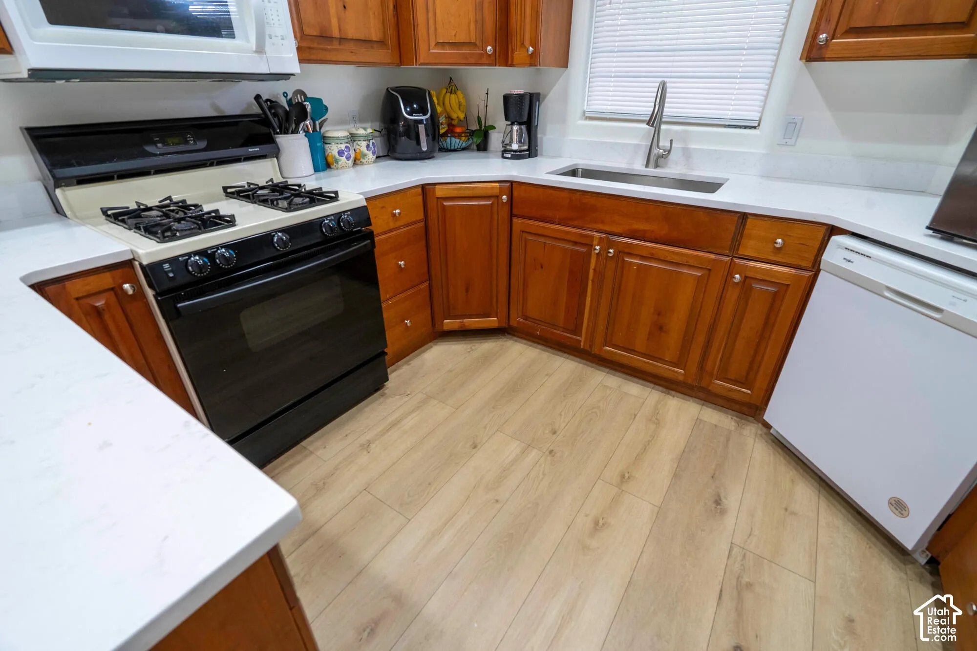 Wood-finish flooring, white countertops, wood cabinetry, black gas range, and white microwave