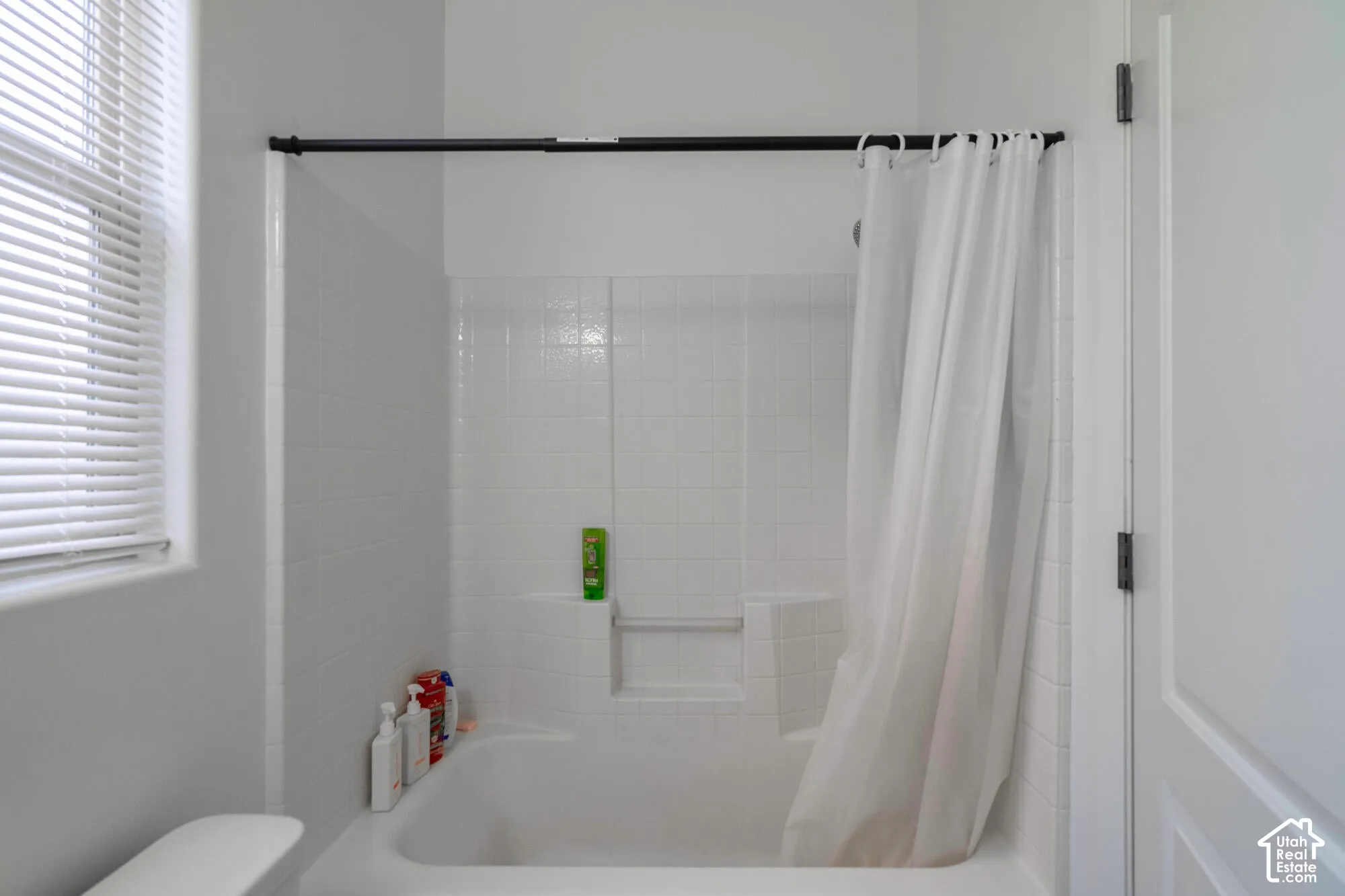 Bathtub with white subway tile surround and integrated shelving, featuring a window with blinds