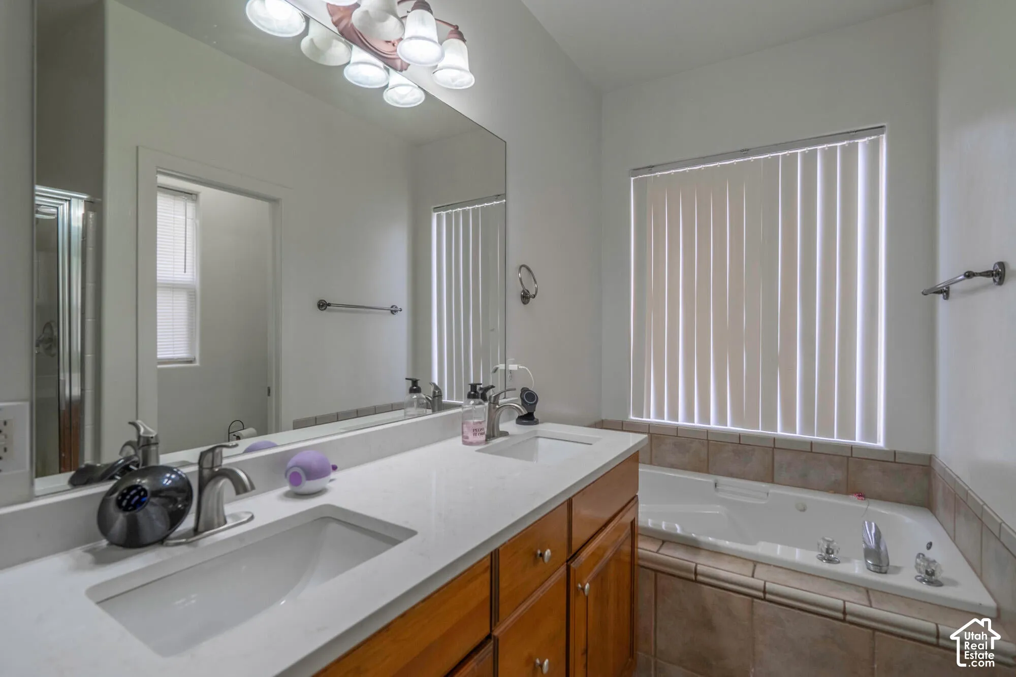 Dual undermount sinks with brushed nickel faucets, a spacious countertop, wood-finish cabinetry, a built-in bathtub with tiled surround, and a large mirror with overhead lighting
