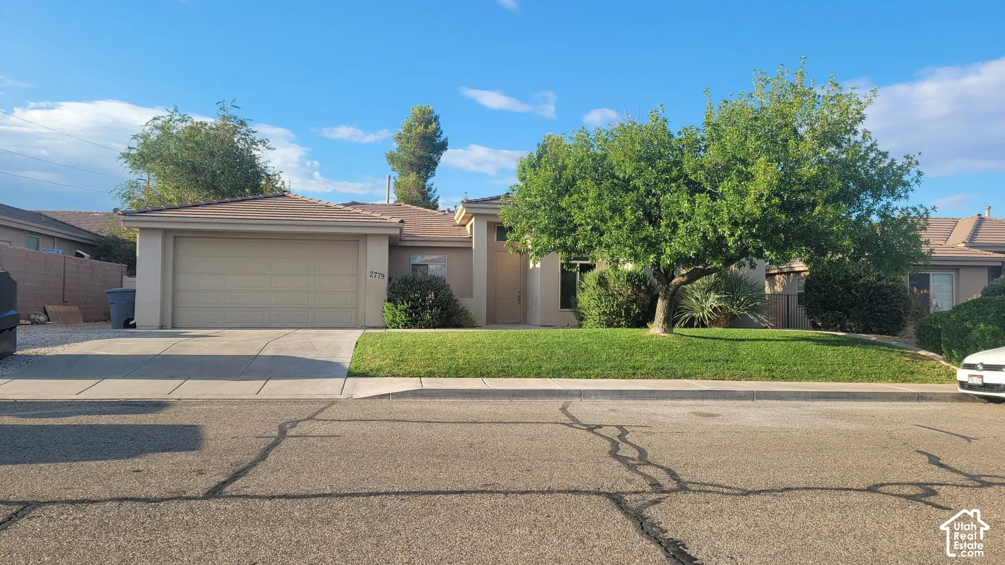 Single-story residence featuring a two-car garage, manicured lawn, and mature trees