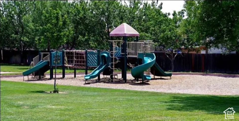Recreational area featuring play structure with slides and climbing elements, surrounded by a wood chip surface and expansive green lawn