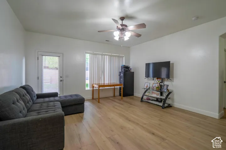 Wood-finish flooring, ceiling fan with integrated lighting, window with blinds, and white walls