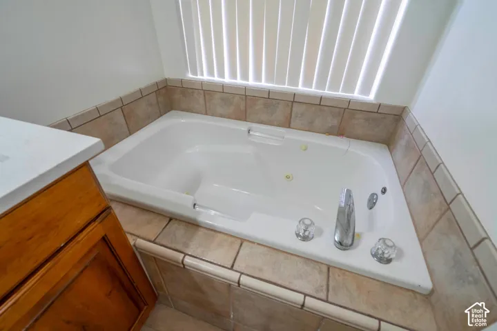 White built-in soaking tub with chrome fixtures, surrounded by neutral-toned tiled decking and wall accents