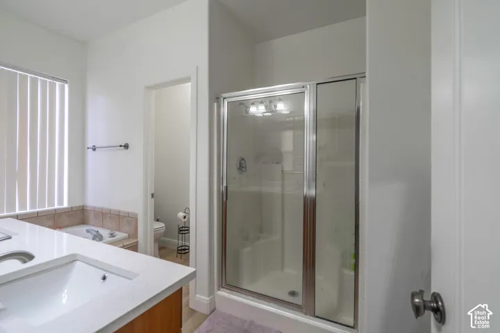 Dual vanity with integrated sinks and white countertops, shower enclosure with clear glass, tiled soaking tub, and vertical blinds