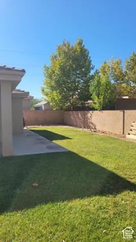 Expansive backyard featuring a manicured lawn, concrete patio, and mature trees