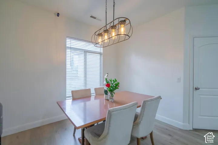 Wood-finish flooring with white baseboards, a single window with blinds, and a modern rectangular chandelier