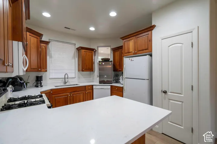 White countertops, wood cabinetry, a gas cooktop, recessed lighting, and light wood-finish flooring