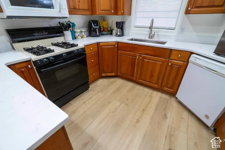 Wood-finish flooring, white countertops, wood cabinetry, black gas range, and white microwave