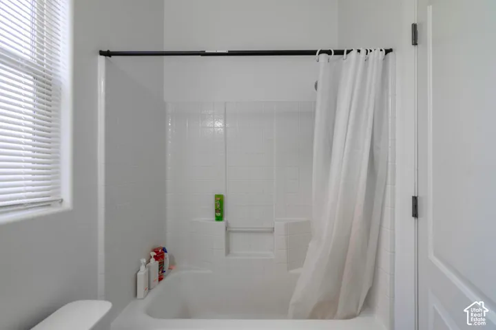 Bathtub with white subway tile surround and integrated shelving, featuring a window with blinds