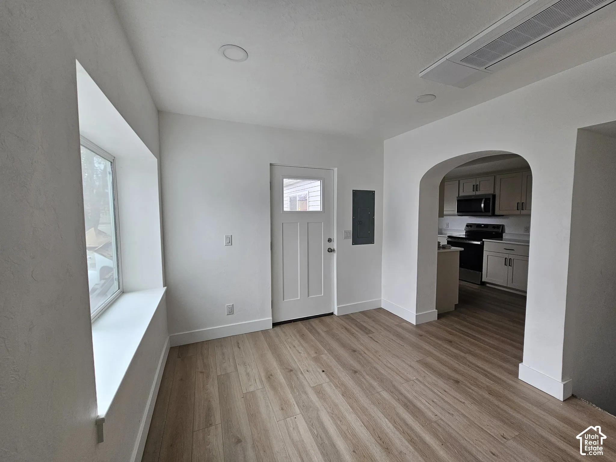 Recessed lighting, wood-finish flooring, broad window with deep sill, arched doorway, and a white paneled entry door