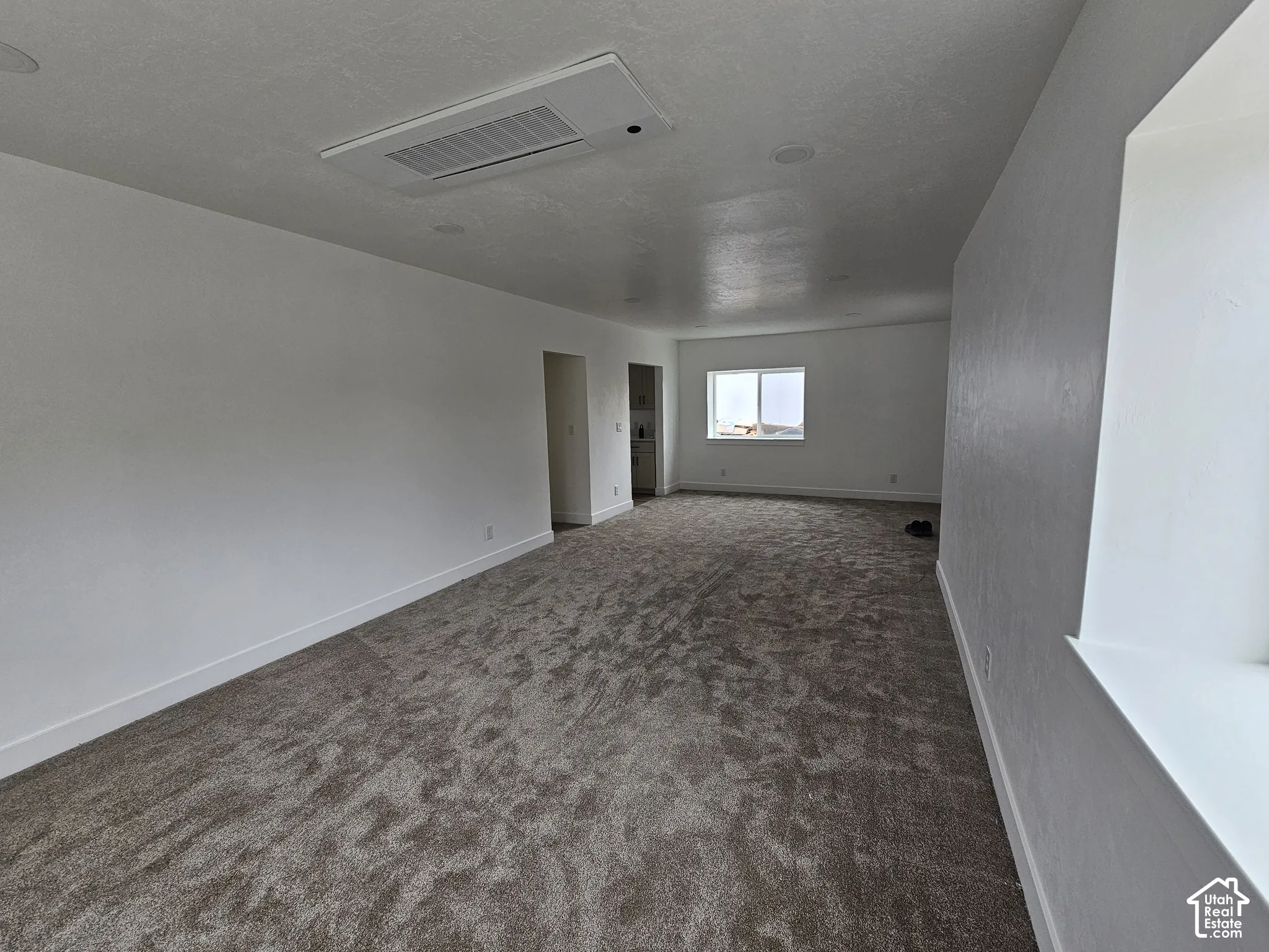 Spacious room with new carpeting, white walls, recessed lighting, and a ceiling-mounted HVAC register