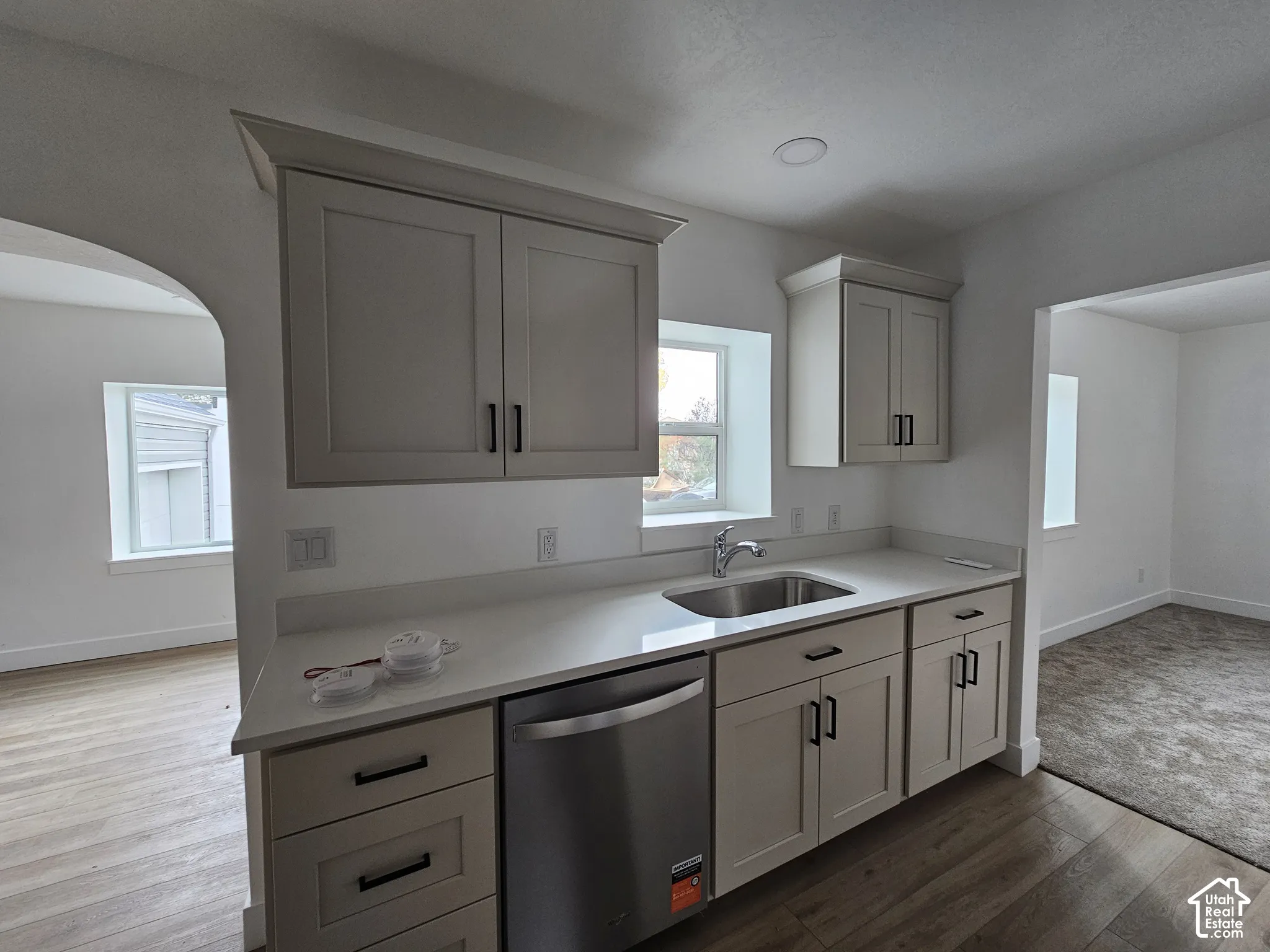 Kitchenette featuring light-toned cabinetry, stainless steel sink, integrated dishwasher, and light-colored countertops