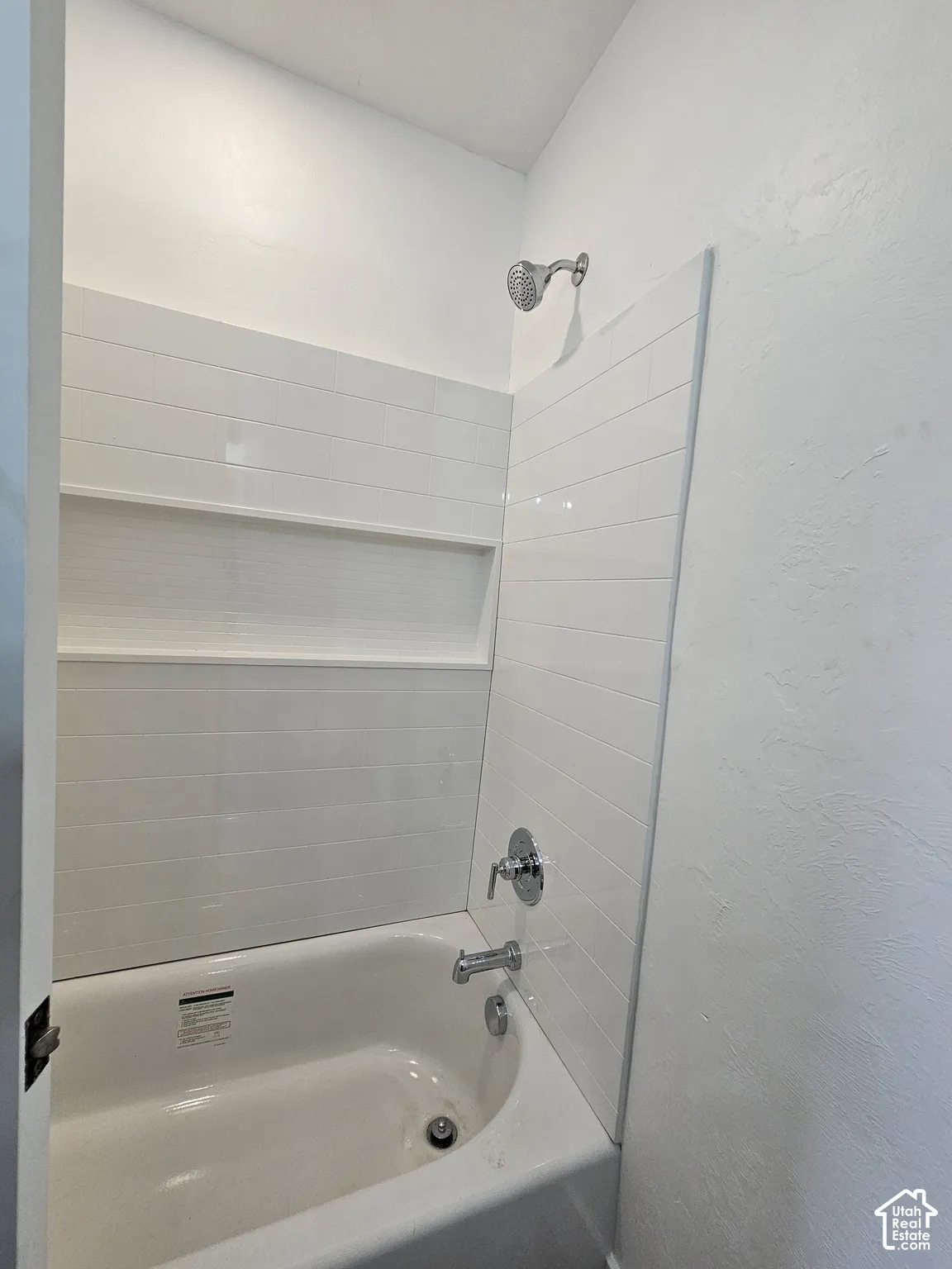 White bathtub with chrome fixtures and horizontally-laid tile surround