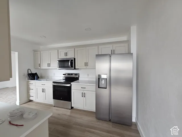 Kitchen featuring white shaker-style cabinetry, stainless steel appliances, a stainless steel microwave, and wood-finish flooring