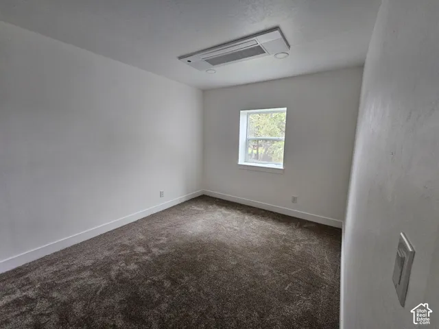 Neutral-toned walls with textured finish, dark carpeting, and a white-trimmed window
