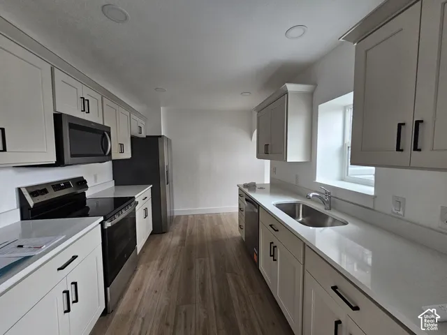 White shaker-style cabinetry with matte black hardware, stainless steel appliances, light-toned countertops, wood-finish flooring, and recessed lighting