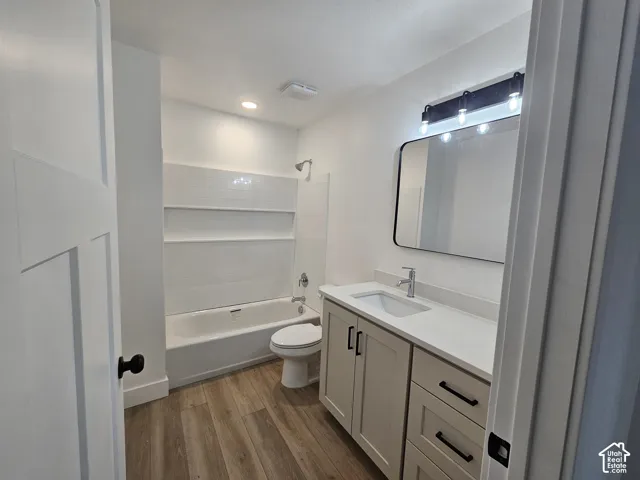 Modern bathroom featuring a single vanity with a white countertop, wood-finish flooring, a white bathtub with tile surround, and a rectangular mirror with black trim