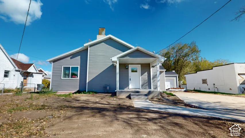 Exterior featuring gray horizontal siding, a covered front entryway, concrete porch, and a chimney