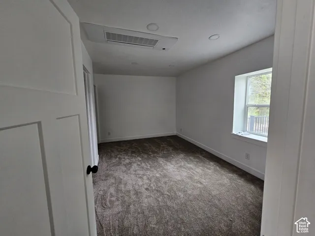 White interior walls, recessed ceiling lighting, large window with white trim, dark textured carpeting, and white interior door with black hardware