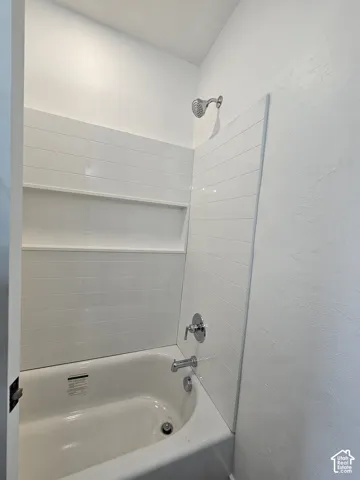 White bathtub with chrome fixtures and horizontally-laid tile surround
